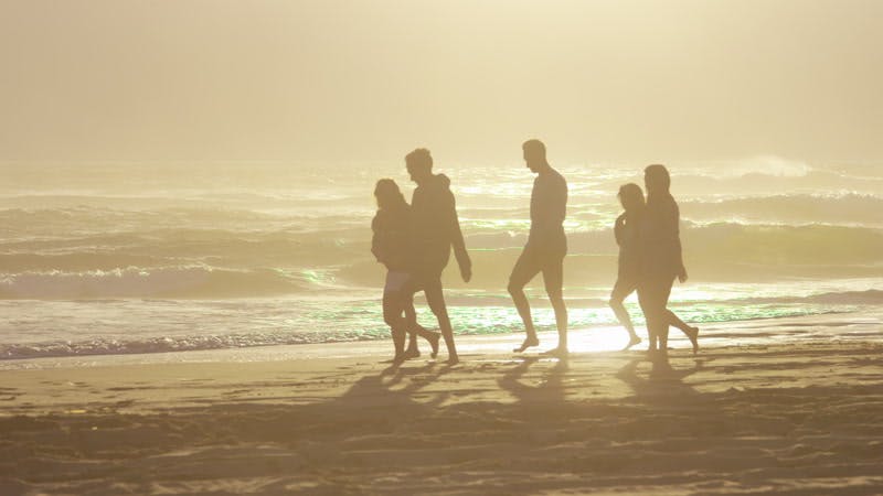 group of people walking on a beach next to the ocean at sunset