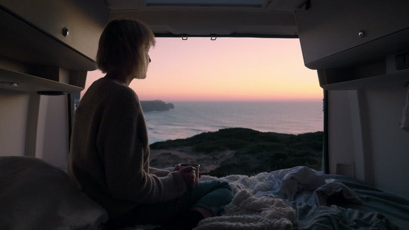 woman drinking from a cup in an open camper van at sunset