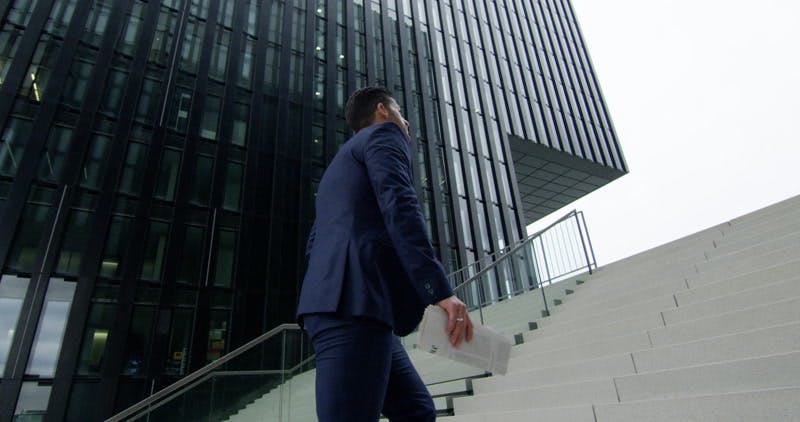businessman walking up stairs while holding newspaper