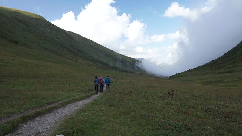 people walking on a trail in a valley with clouds 