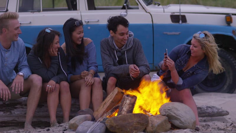 group of people taking photos of themselves while sitting outside next to a campfire