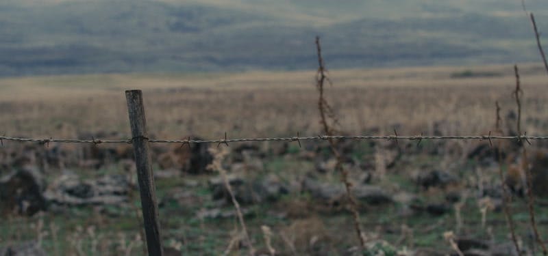 Barbed wire on fence in front of open field and mountain