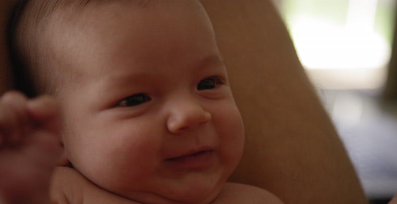 baby smiles and shakes hands while leaning on adults legs 