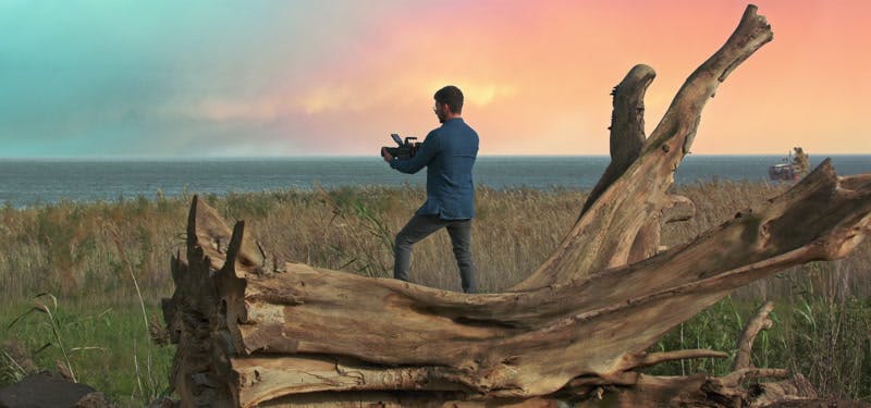 cameraman standing on log and recording ocean