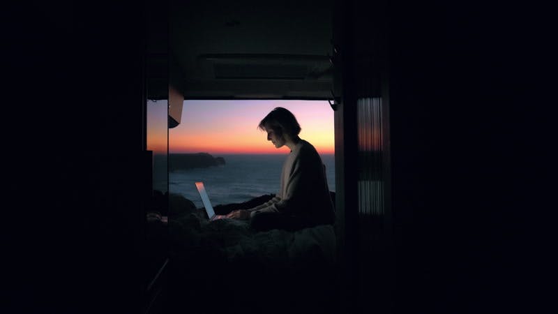 woman typing on a laptop in an open camper van on the sea coast at sunset