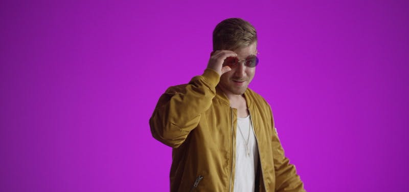 male model taking off sunglasses and showing his tongue with purple background