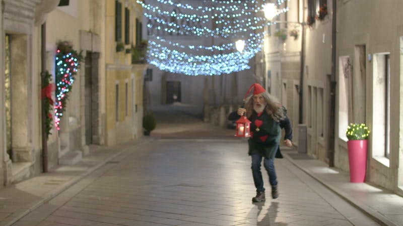 man dressed as an Christmas elf while carrying a lantern in a decorated street