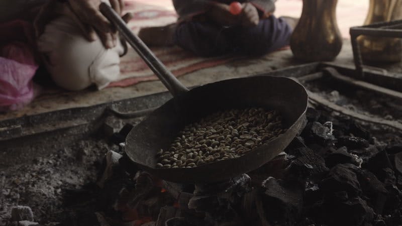 person cooking nuts on fire in pan over charcoal