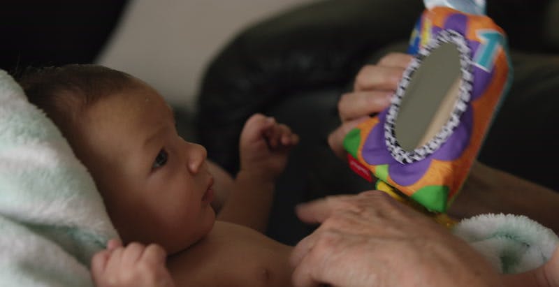 baby with confused expression is shown a toy mirror 