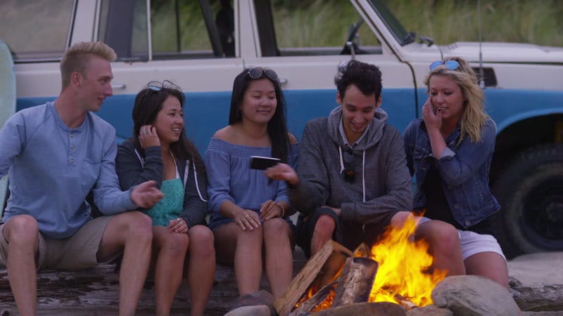 man photographing a group of people photo next to a campfire 