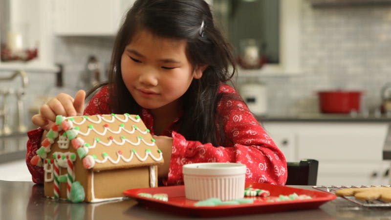 little girl decorating a gingerbread house and smiling