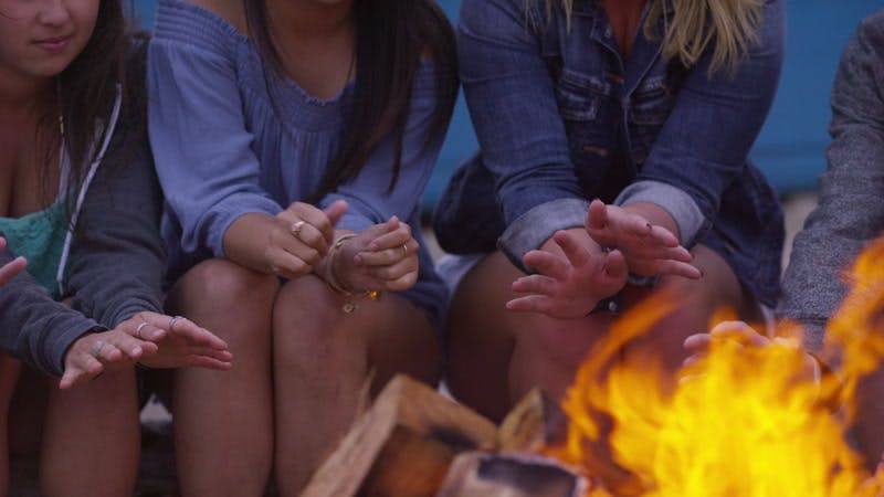 group of people sitting around a camp fire and warming themselves outdoors