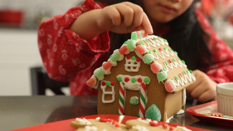little girl decorating a gingerbread house with gumdrops 