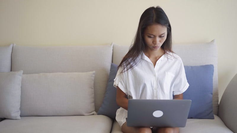 woman sitting on couch typing on laptop