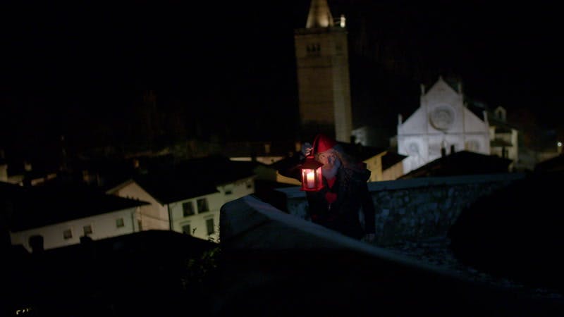 bearded man dressed in an elf hat and carrying a lantern on a rooftop at night