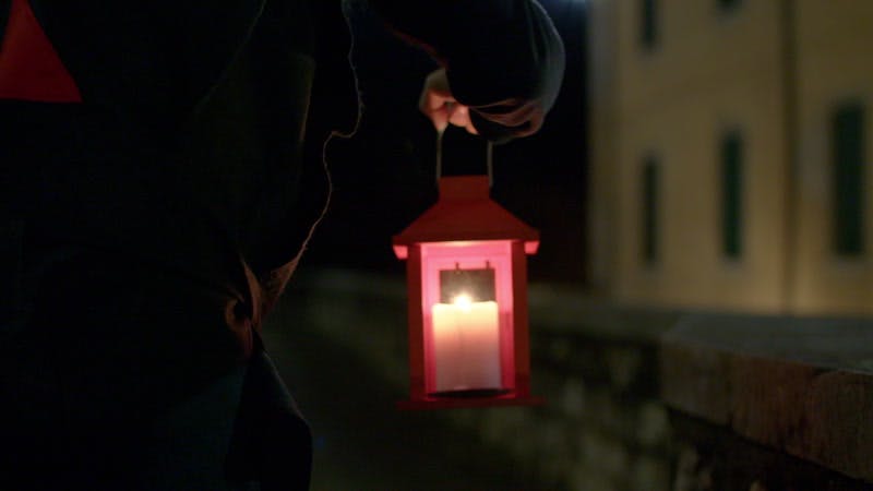 person carrying a lantern near buildings at night