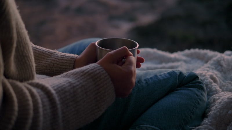 woman drinking from a cup outdoors near the sea at sunset