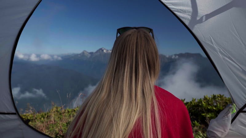 woman sitting in a tent and looking at the mountains 