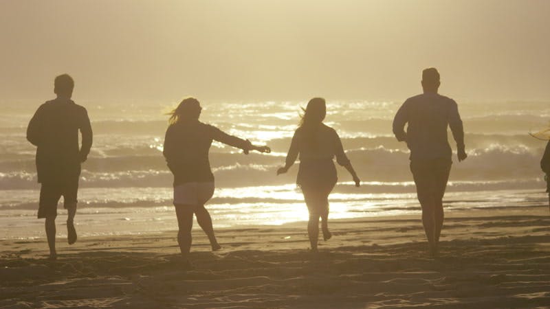 five people running towards the sea on a beach at sunset