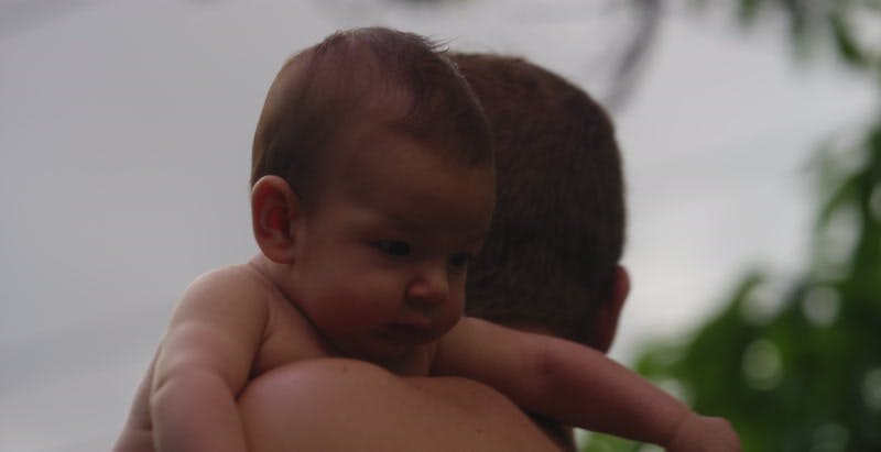 father holding baby over shoulder turns around to look to side