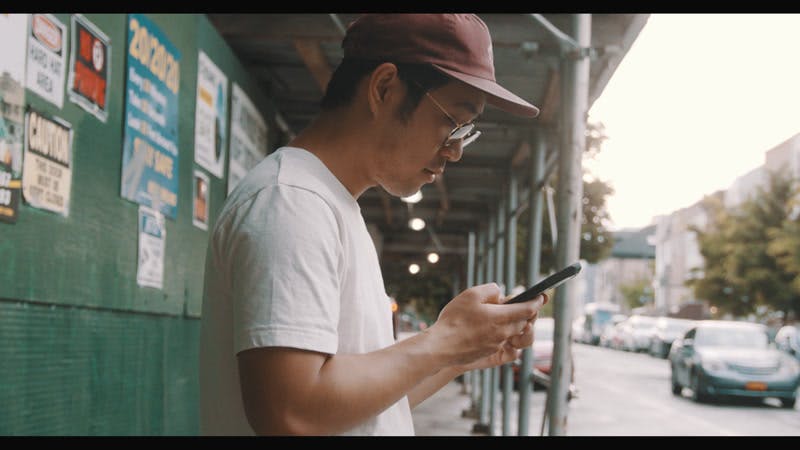 man typing on cellphone then talks and looks straight at camera in city