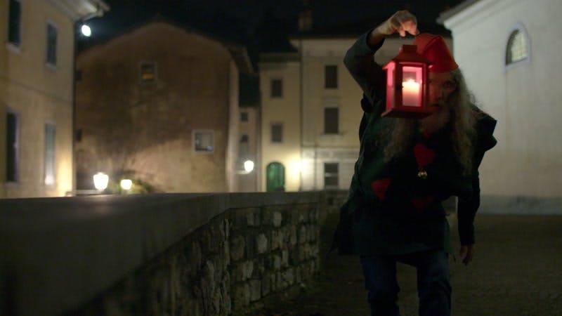 person dressing as an elf and carrying a lantern near town buildings at night