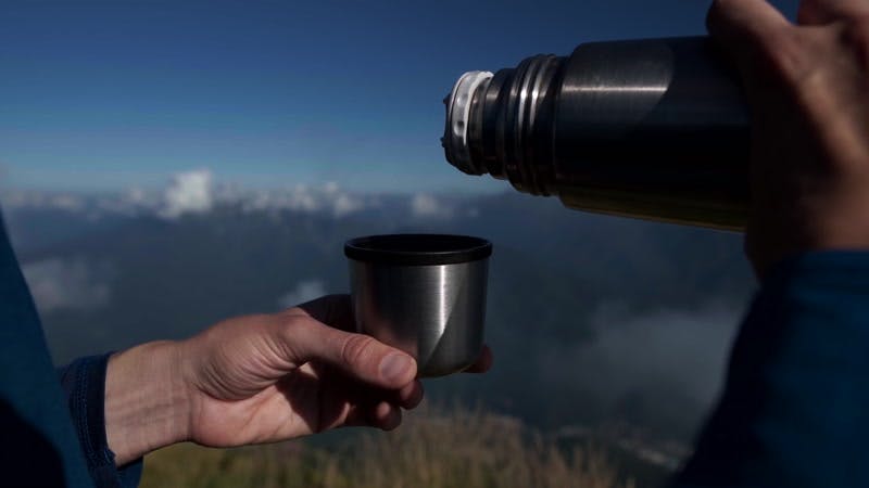 man pouring tea into a cup in the mountains 