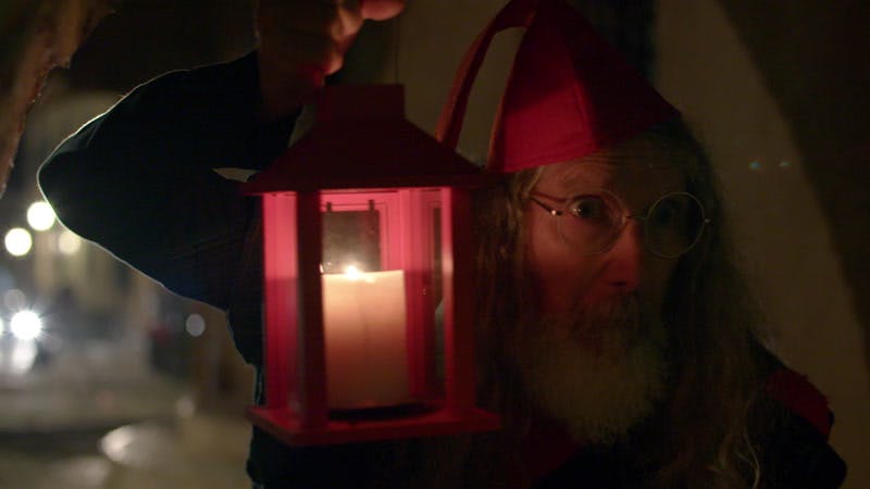man with a beard wearing a red hat and carrying a lantern at night