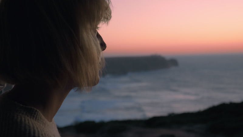 woman drinking from a flask cup on the coast at sunset