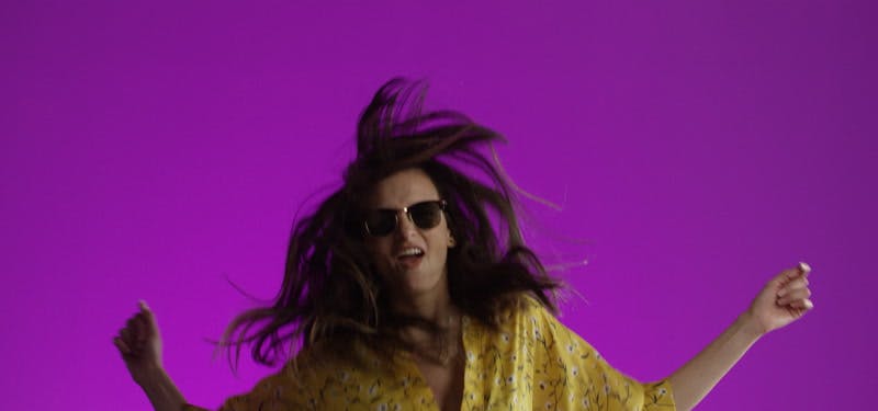 young model jumping with sunglasses in front of purple background