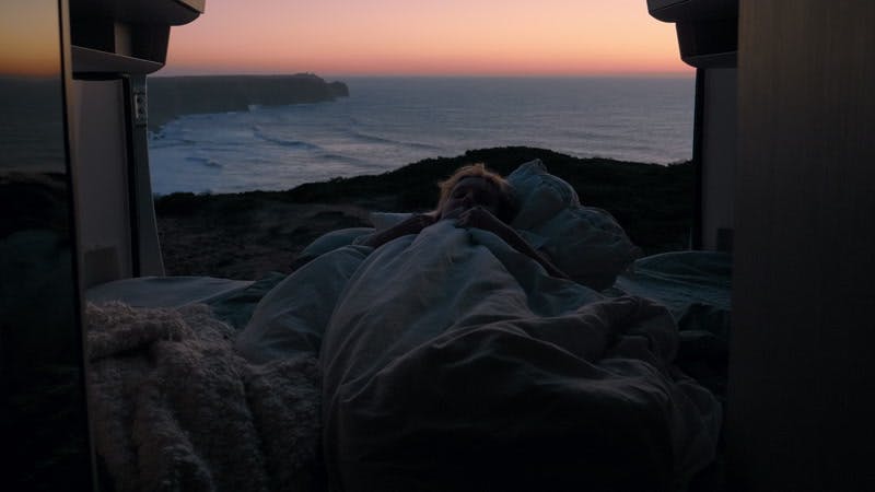 woman lying down in an open camper van on the sea coast at sunset