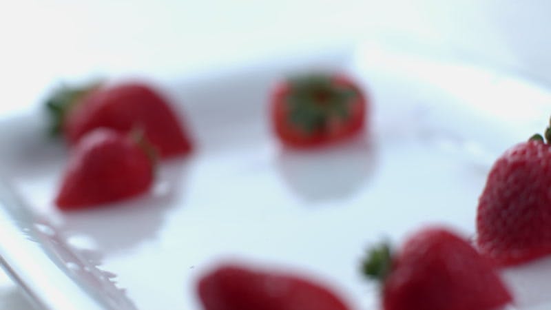 strawberry falling into a dish with water and more strawberries 